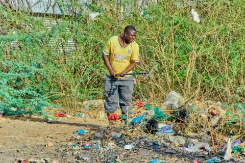 A volunteer clearing overgrown bush and rubbish with a rake