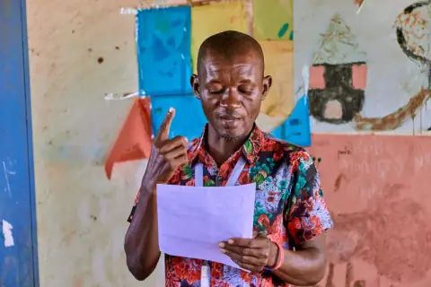A man reading from a sheet of paper while addressing a meeting